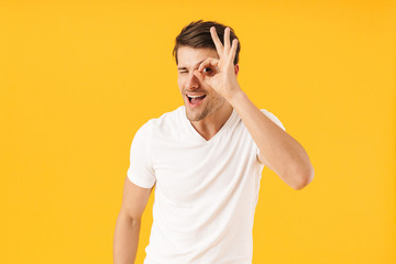 Photo of cheery man in basic t-shirt smiling at camera while showing ok sign