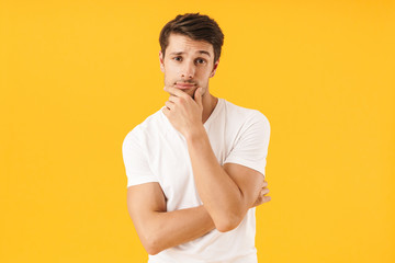 Photo of attractive man in basic t-shirt touching his chin and looking at camera with pensive face