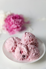 Balls of berry ice cream on a plate and white and pink peonies on a white background side view