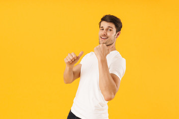 Photo of positive man in basic t-shirt smiling and gesturing fingers at copyspace