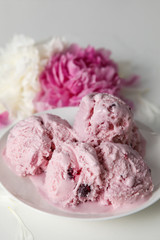 Balls of berry ice cream on a plate and white and pink peonies on a white background side view