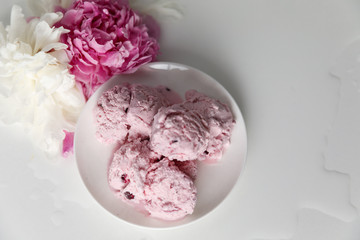 Balls of berry ice cream on a plate and white and pink peonies on a white background top view, copy space