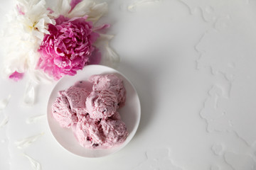 Fototapeta na wymiar Balls of berry ice cream on a plate and white and pink peonies on a white background top view, copy space