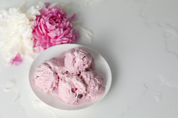 Balls of berry ice cream on a plate and white and pink peonies on a white background side view, copy space