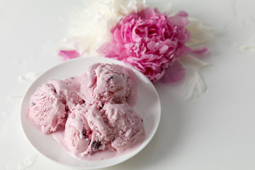 Balls of berry ice cream on a plate and white and pink peonies on a white background side view