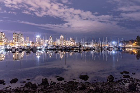 Vancouver, BC \ Canada - 13 March 2019: A night long exposure photo of marina inside Burrard Inlet of Vancouver Harbor with many yachts and boats against colorful illuminated city skyline