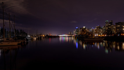 Vancouver, BC \ Canada - 13 March 2019: A night long exposure photo of marina inside Burrard Inlet of Vancouver Harbor with many yachts and boats. Lights of Canada place are in the background