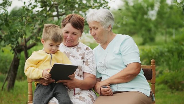 Two grandmothers and grandson playing games on the tablet