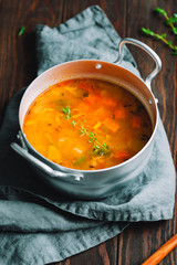 Spring vegetable soup with chicken stock in a pot on kitchen wooden table. Rustic style, close-up view.
