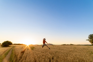 Boy jumping in the a wheat field, with shorts and orange sweater. The sky is blue