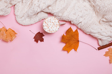 Autumn composition with knitted sweater, cocoa with marshmallows and yellow leaves on pink...