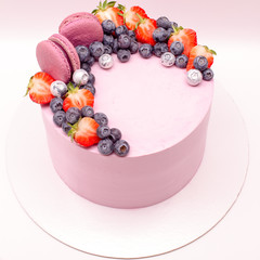 Delicious pink cake decorated with macaroons, strawberries, silver blueberries. On a white background.