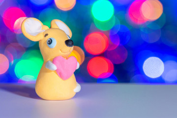 Beautiful cute toy rat made of plasticine on the background of Christmas lights from the garland
