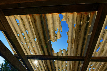 The sky is showing through the holes in the corrugated roof