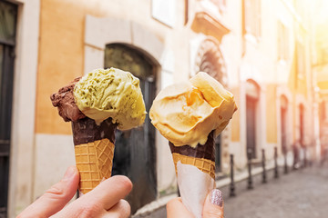 Two hands close-up holding cones with italian ice-cream gelato on the background of Rome streeet - obrazy, fototapety, plakaty
