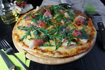 Pizza with bacon, cheese and herbs on a wooden dish on a black wooden background