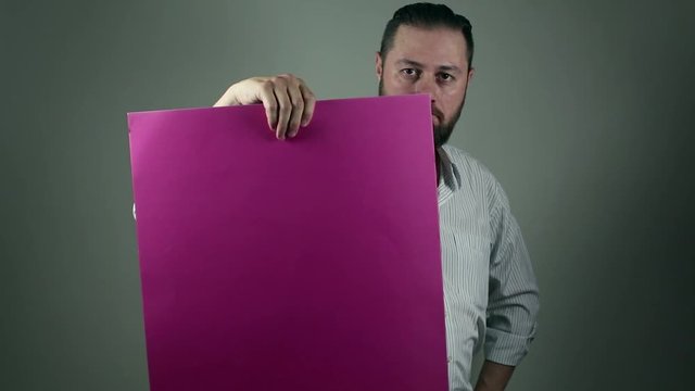 Casual beard man holding a purple cartboard to write something on it. Points vigurosly at the board to pay attention. News and announcement