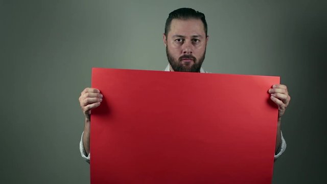 Casual beard man in shirt rising a red cartboard to write something on it. Funny face while holding an announcement board. News or business list or to do lists