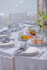 Making a table for a holiday with snacks for guests with bouquets of different flowers and candlesticks with glasses on the background of the sea.