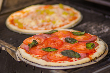 Cooking traditional Italian pizza with tomatoes mozzarella cheese sausages and ham on the grill