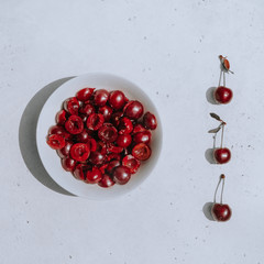 Cut halves of ripe berries of dark red cherry in white bowl next to whole berries on white background