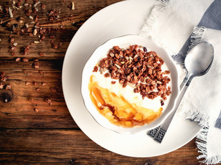 Joghurt, selbstgemachtes Granola und Honig in einer weißen Schüssel, rustikaler Stil, brauner Holztisch, Flat lay