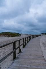 Fototapeta na wymiar Holzsteg mit Sanddünen und Gewitterwolken