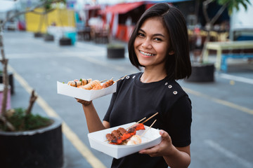 Asian young woman carrying a street food grilled with skewers