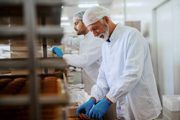 Two hard working food plant employees in sterile uniforms packing cookies in boxes.