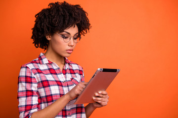 Close-up portrait of nice cute attractive smart clever intelligent wavy-haired lady wearing checked shirt using digital e-book hobby isolated over bright vivid shine orange background