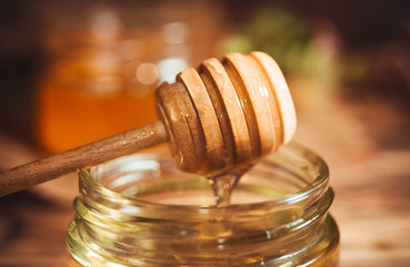 Fresh summer honey in glass jar and wooden honey dipper on rustic background