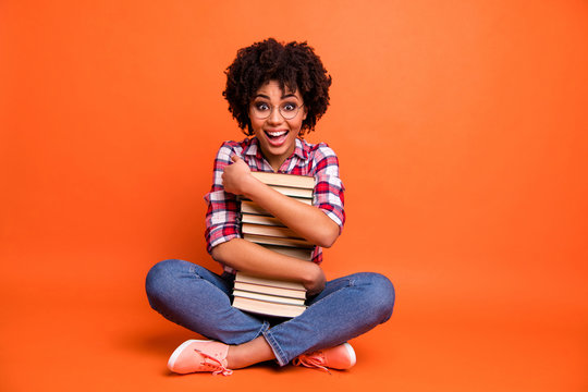 Full body photo pretty curly beautiful lady sit floor hold hands books free time wait reader wear specs casual checkered plaid shirt isolated orange background