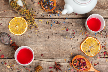 cups of healthy herbal tea with cinnamon, dried rose and camomile flowers in spoons over wooden background, top view