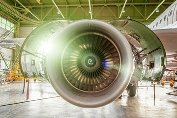 Aviation maintenance inside hangar with a flash light inspects airplane engine.