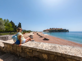 Budva, Montenegro. Girl near Sveti Stefan island. Happy blonde traveler.