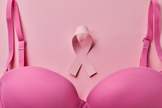 top view of brassiere near ribbon on pink background, breast cancer concept
