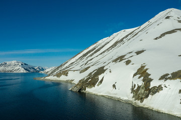 The mountainous sea coast covered with snow in a sunny weather.