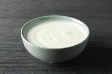 Obraz na płótnie Canvas Bowl of sour cream yogurt on dark wooden background