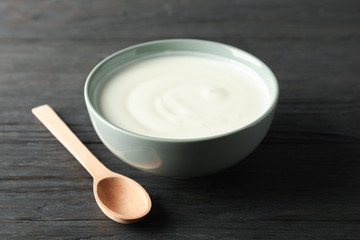 Bowl of sour cream yogurt and spoon on wooden background