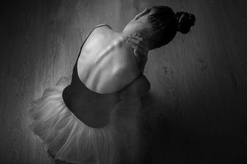 Tight back exhausting workouts and pain. Ballet dancer sits on the floor in dark lighted room stretches neck. Top view photo. Horizontal. Copy space