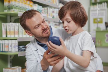 Close up of a mature male pharmacist helping little boy choosing shampoo to buy. Cute little boy talking to the chemist, shopping at drugstore