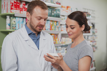 Obraz premium Attractive young woman talking to the chemist, shopping for medicament at the drugstore. Mature male pharmacist helping his female client