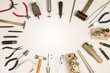 Top view of hands holding goldsmiths tools, jewelry objects. Tools over white background.