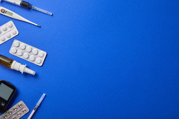 top view of blister packs, nasal spray, thermometer, glucometer and syringes isolated on blue