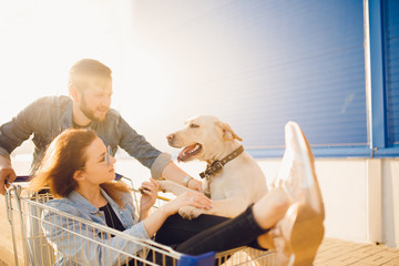 Happy couple having fun supermarket. Young man pushing shopping cart with girfriend and dog