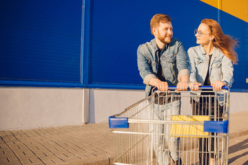 Young man and woman hold cart for products, look at each other and smile. Concept family trip...