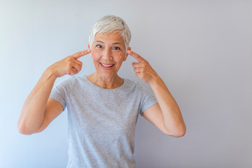 Attractive youthful woman in her fifties applying skin cream or moisturiser to her cheek bone in a...