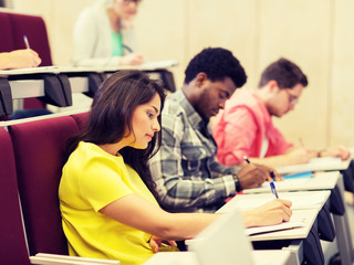 education, high school, university, learning and people concept - group of international students with notebooks writing in lecture hall