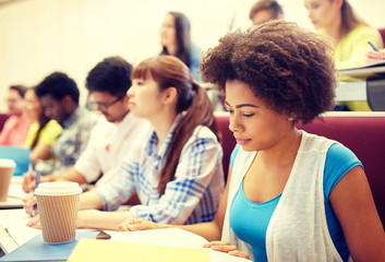 education, high school, university, learning and people concept - group of international students with notebooks and coffee writing test in lecture hall