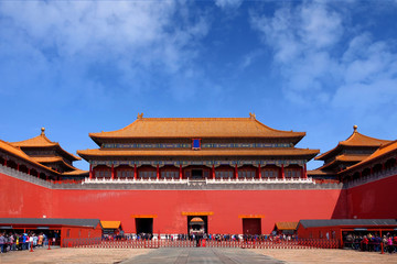 Fototapeta premium People queuing in front of one of the internal red colored gates of the Palace Museum, known as the Forbidden City, in Beijing, against a blue sky.